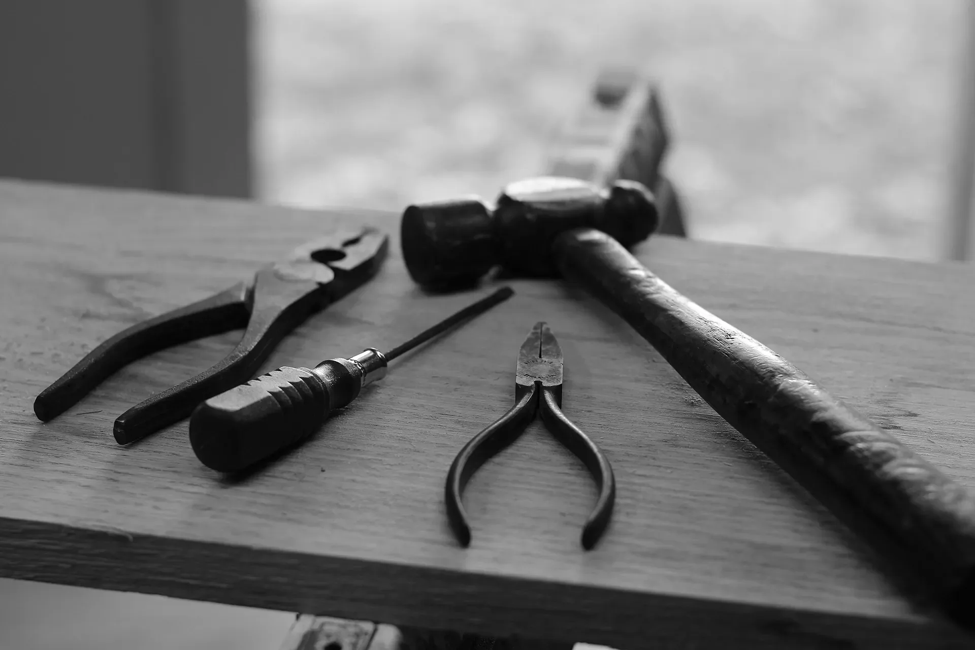 Hammer, pliers, and screwdriver resting on a wooden workbench