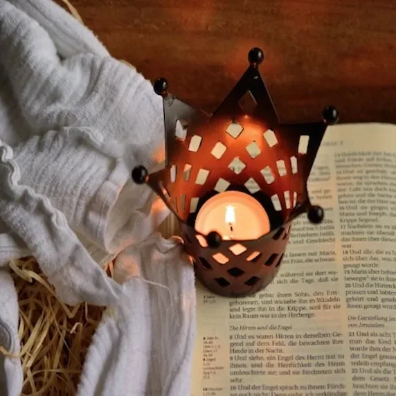 Lit Christmas candle beside an open Bible and white cloth, creating a warm and peaceful holiday scene